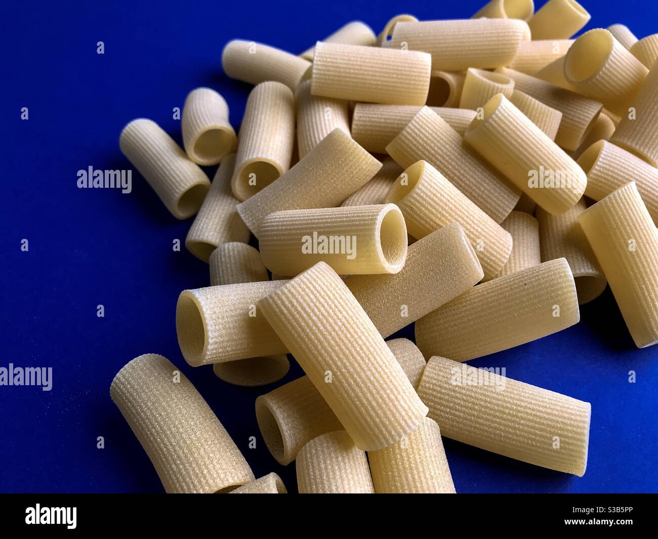 paccheri macaroni Italian dry raw pasta bronze drawn, pasta from Gragnano, Naples,Italy on blue background top view - Smartphone Captured Stock Image