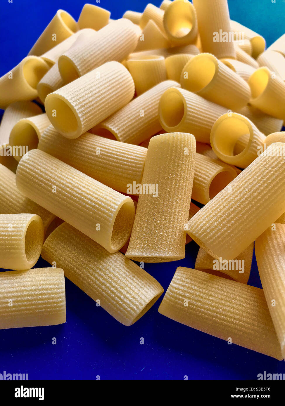 paccheri macaroni Italian dry raw pasta bronze drawn, pasta from Gragnano, Naples, Italy on blue background top view - Smartphone Captured Stock Image