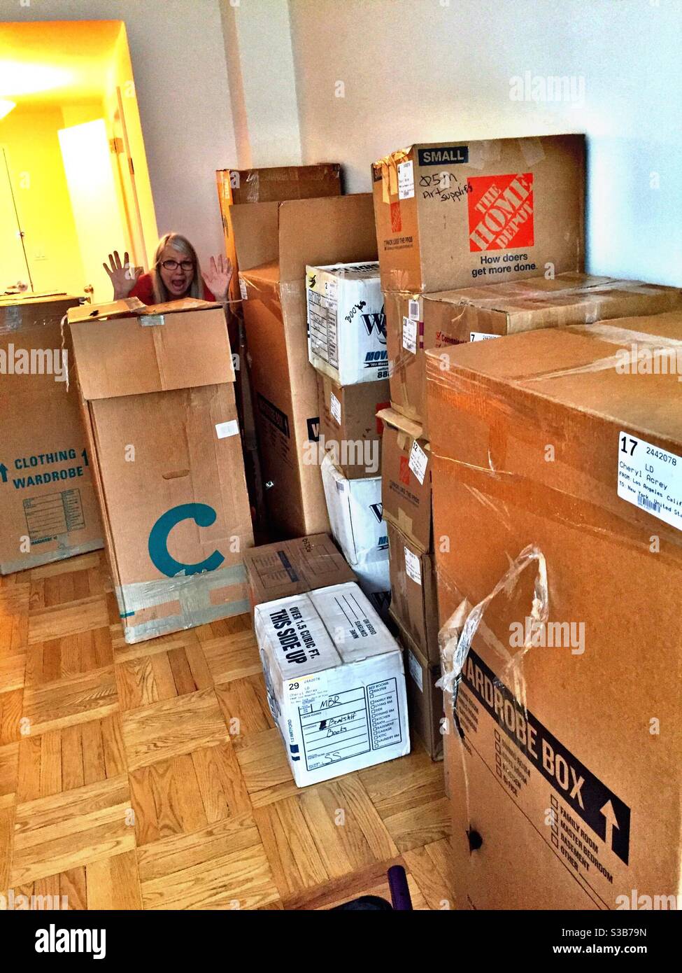 Woman humorously waving from an overwhelming stack of moving boxes, USA - Smartphone Captured Stock Image