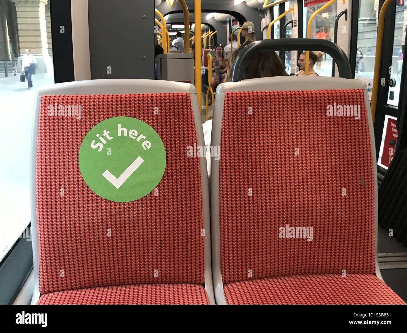Sit here sticker on light rail train seat to encourage social distancing during the COVID-19 (coronavirus) pandemic in Sydney, Australia - Smartphone Captured Stock Image