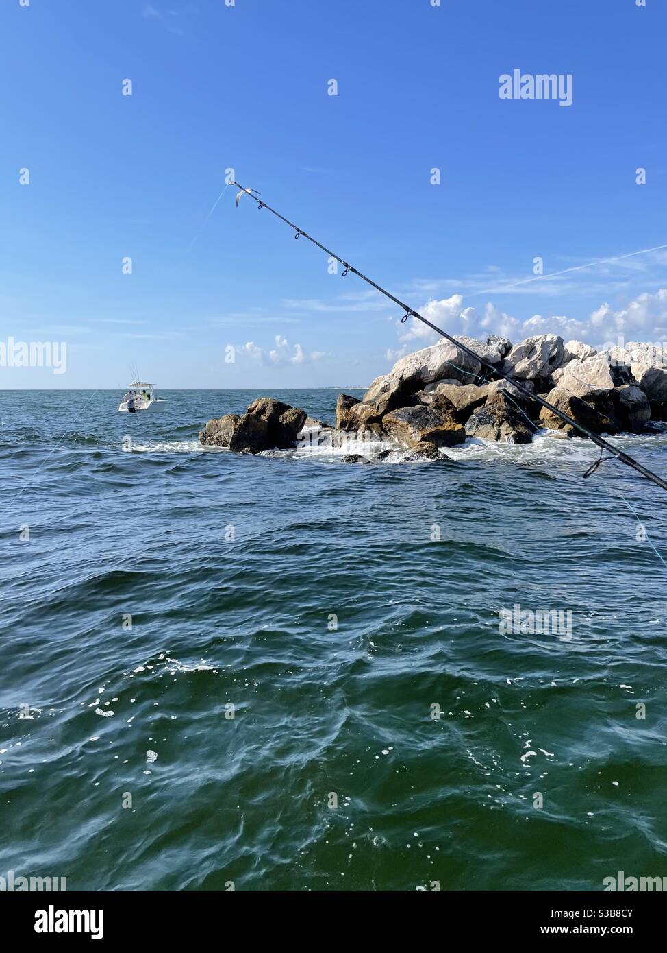 Fishing rod, boat, and rocky jetty at East Pass Destin, Florida, boat view - Smartphone Captured Stock Image