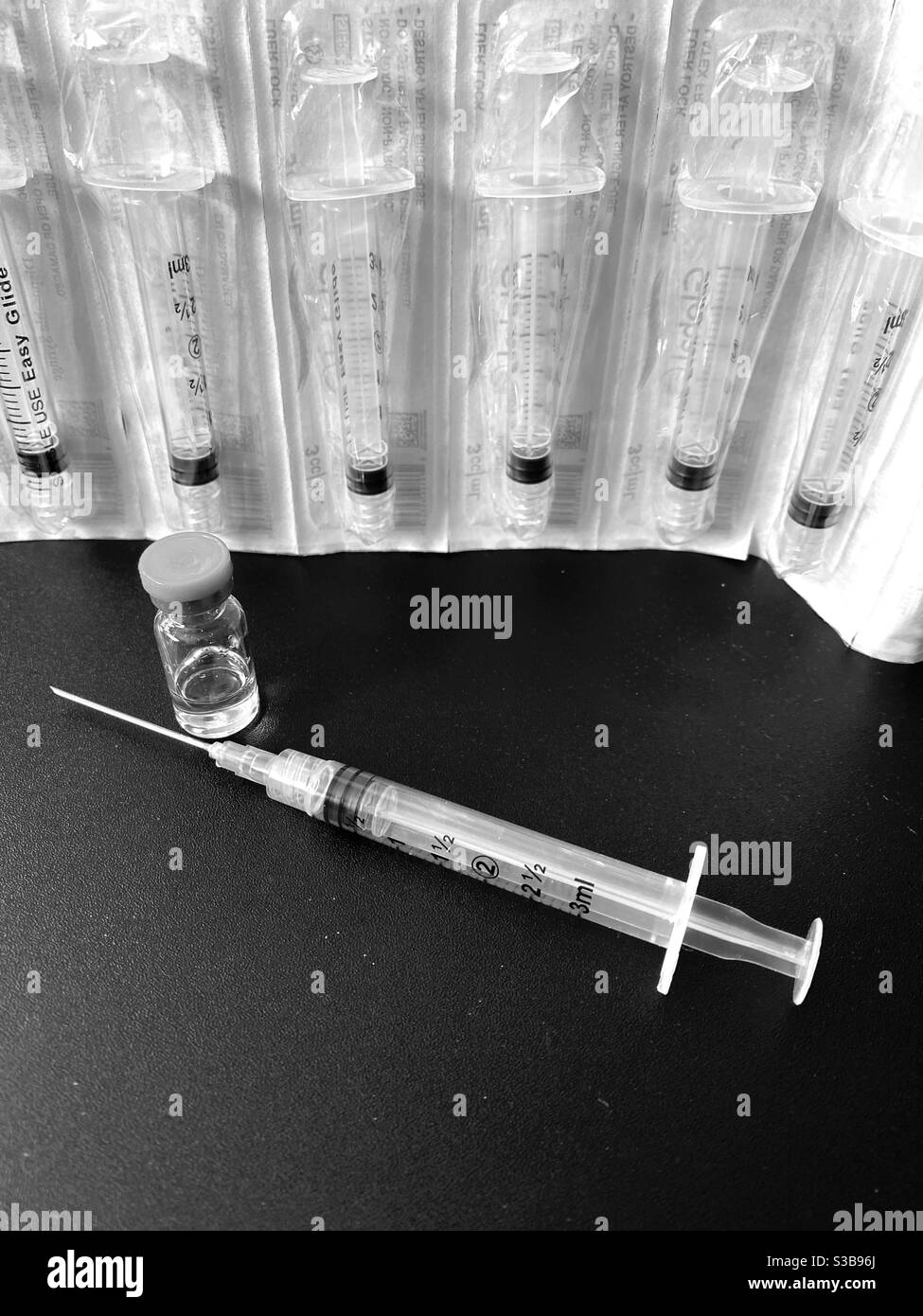 Black and white photo of vaccine vial, needle, and syringes Stock Photo