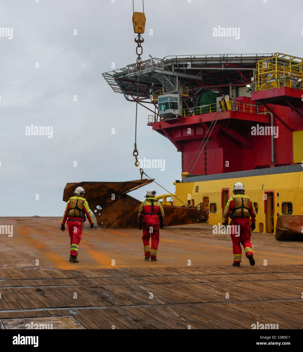 Deckhands walking down deck to disconnect a anchor from the crane Stock Photo