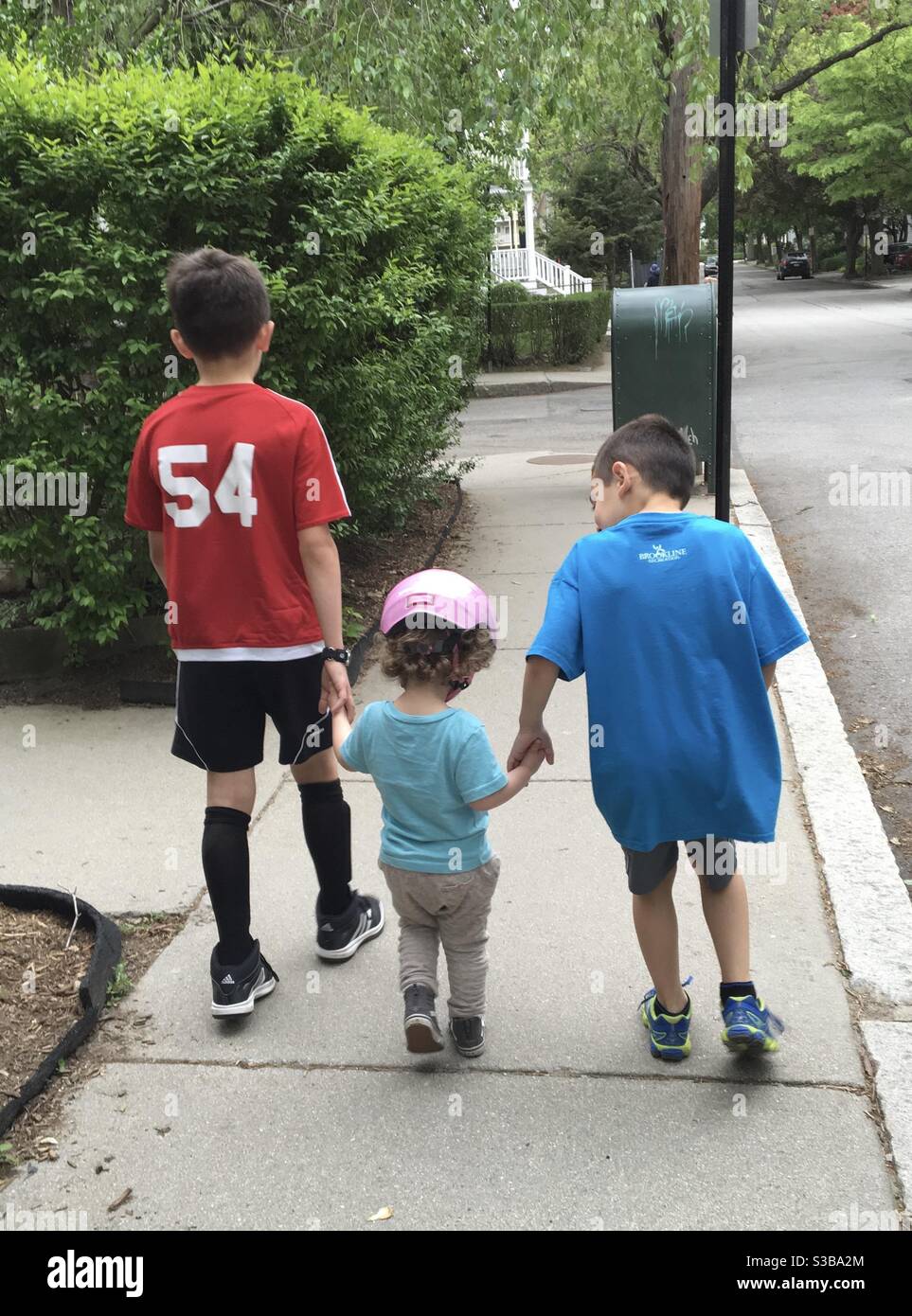 2 young brothers walking their Toddler girl cousin outdoors from behind. Stock Photo