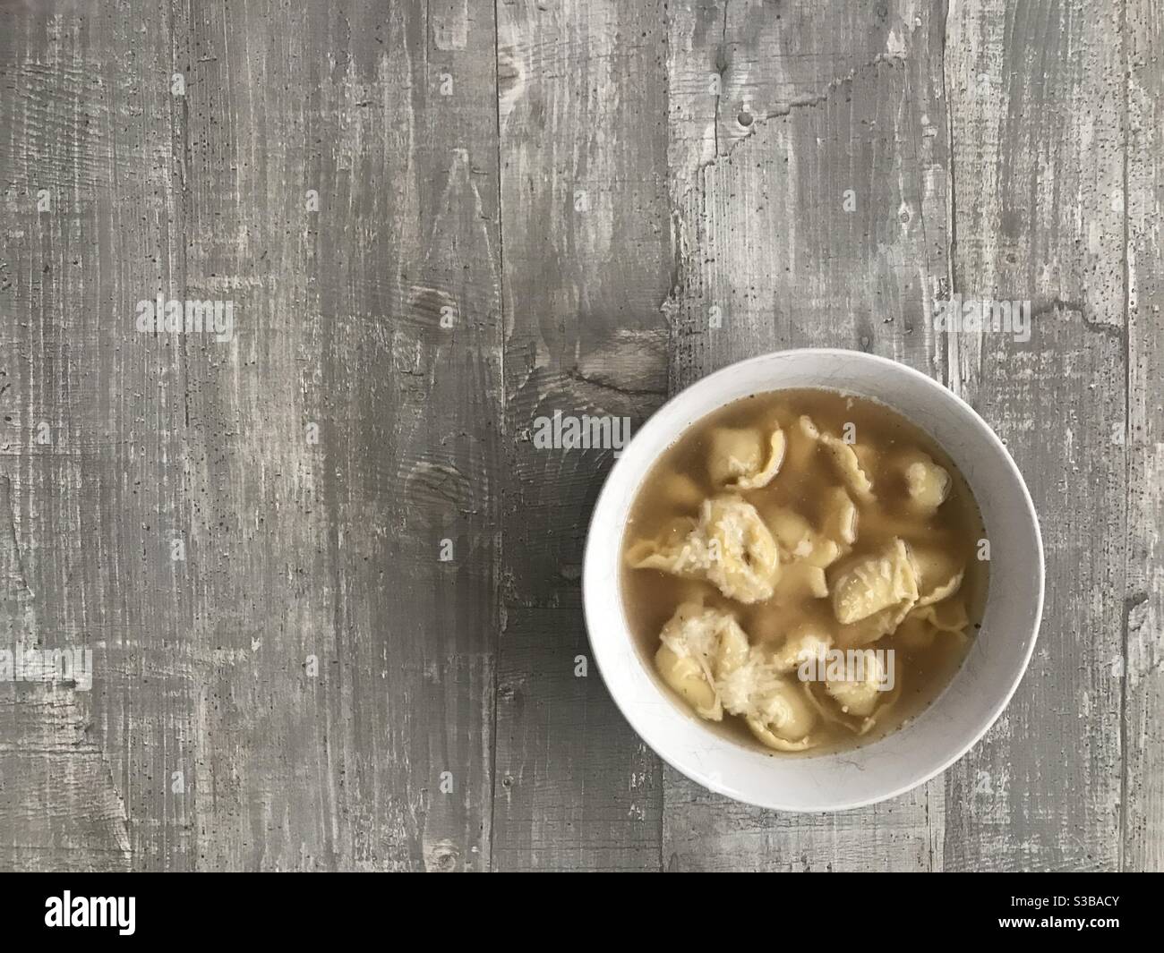 A bowl of cappelletti meat filled pasta in chicken broth on a wooden background - Smartphone Captured Stock Image