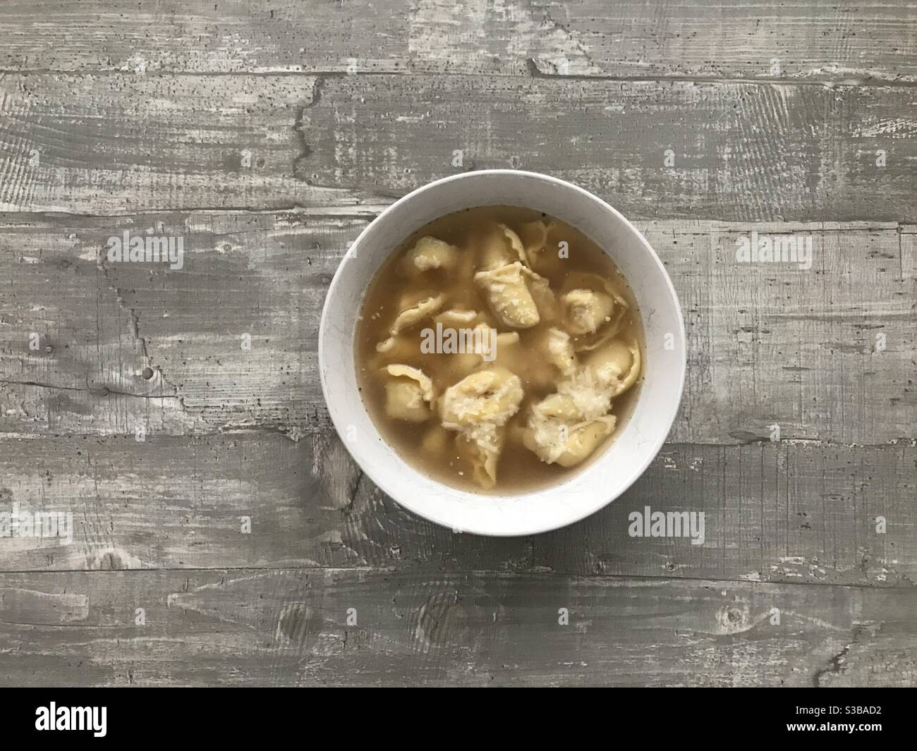 A bowl of cappelletti meat filled pasta in chicken broth on a wooden background - Smartphone Captured Stock Image