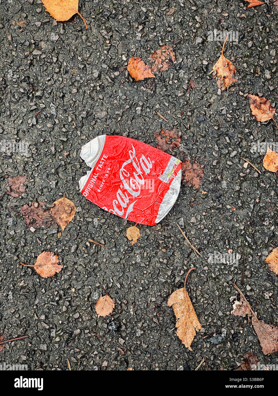 An overhead picture of a squashed Coca-Cola can. Discarded litter, thrown onto a tarmac path. Dead, Brown leaves means it’s autumn. Photo Credit - ©️ COLIN HOSKINS. Stock Photo