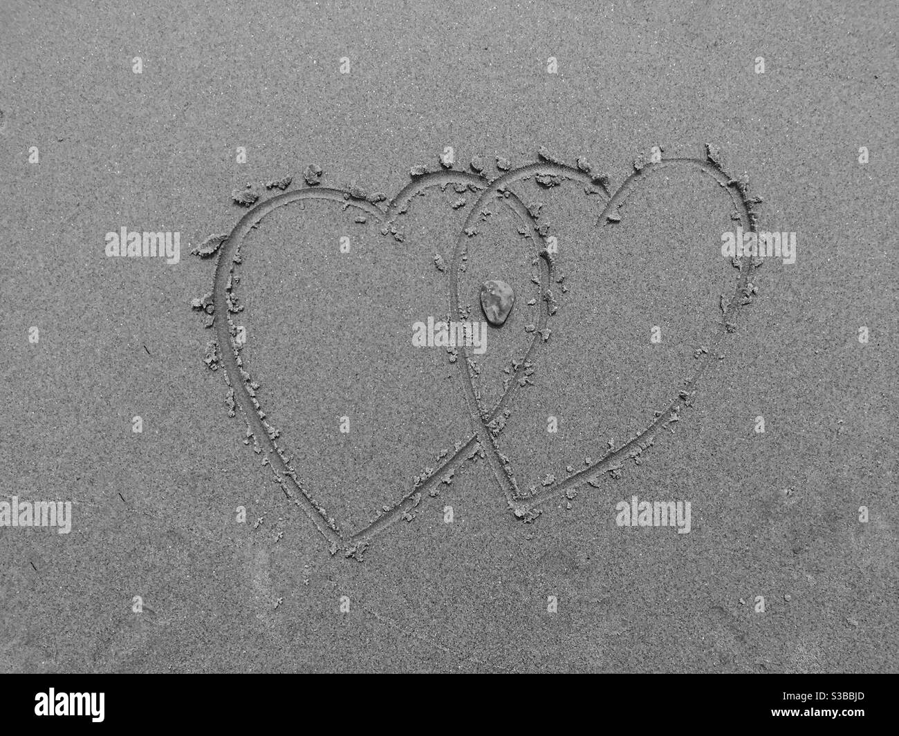 Hearts in sand. Rock in the intersection symbolizes a flinty heart. Concepts: heart matters, line in the sand, iconic, symbols, connected, love. Beach, Halifax, Canada - Smartphone Captured Stock Image