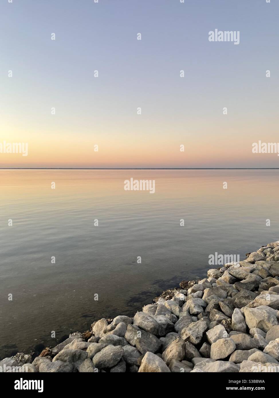 Soft pastel sunset skies with rocky shoreline over the Choctawhatchee ...