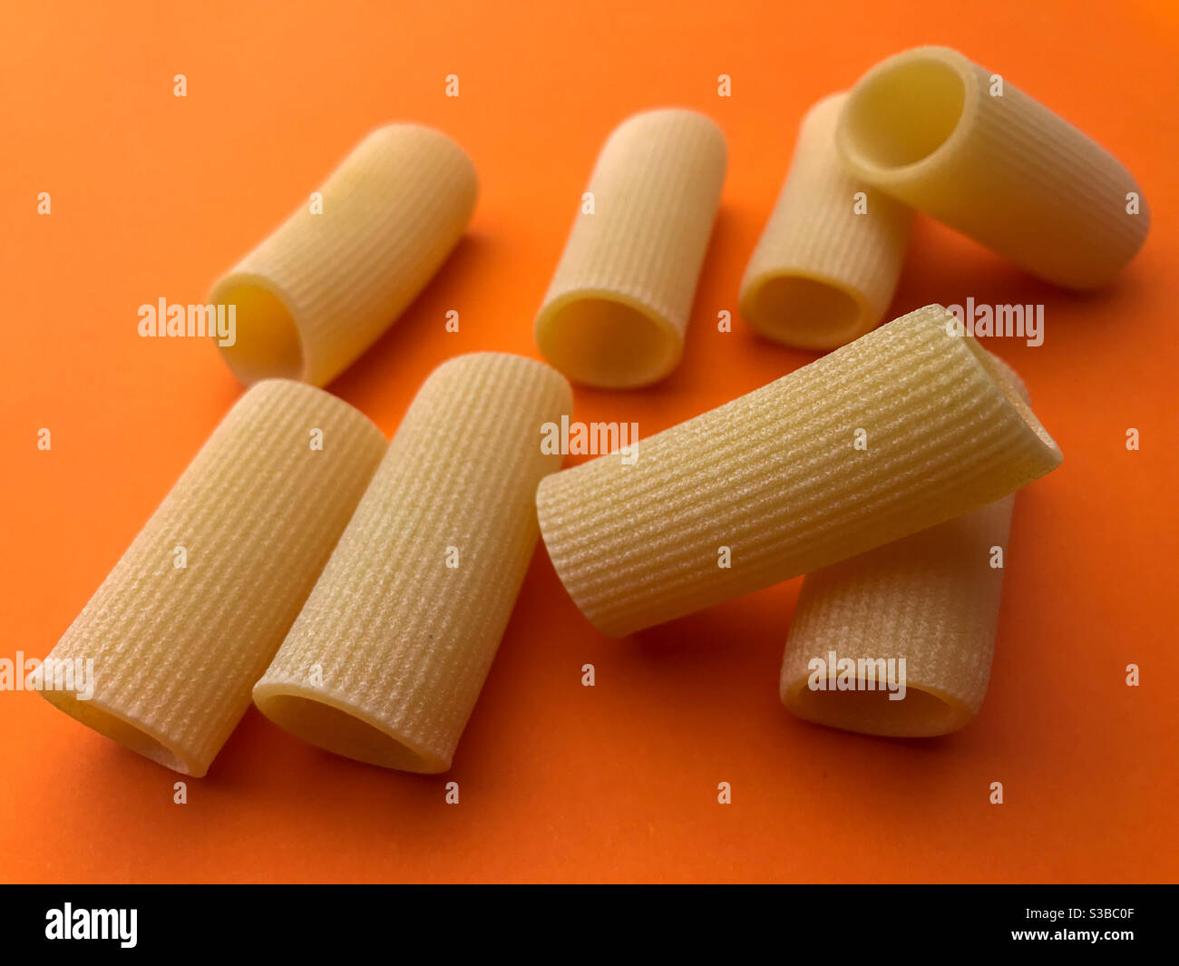 paccheri macaroni Italian dry raw pasta bronze drawn, pasta from Gragnano, on orange background top view - Smartphone Captured Stock Image