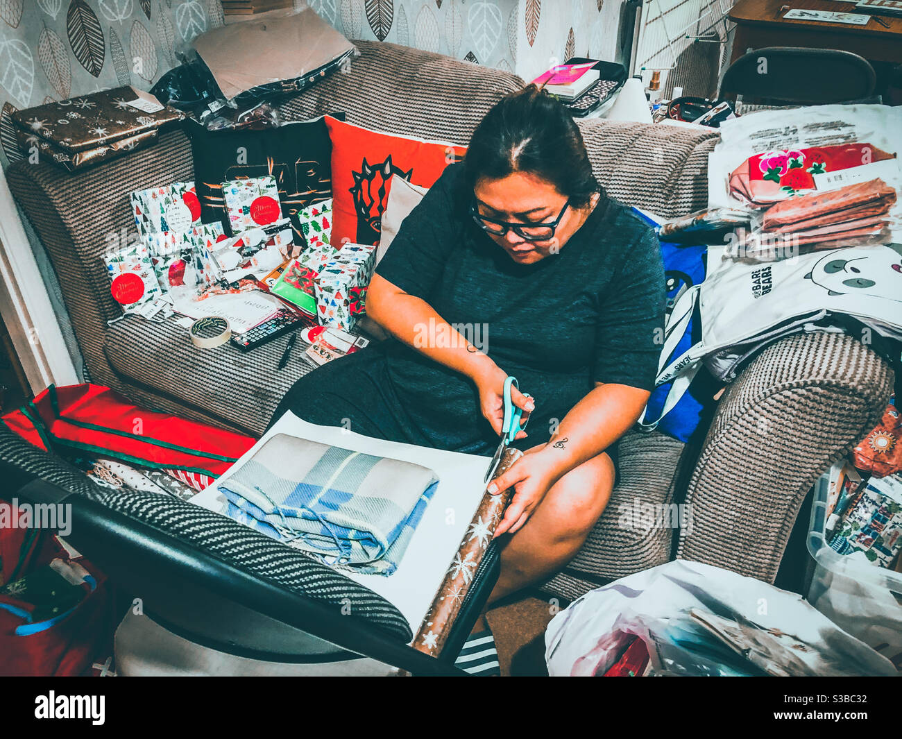 A lady wraps Christmas presents sat on a sofa. - Smartphone Captured Stock Image