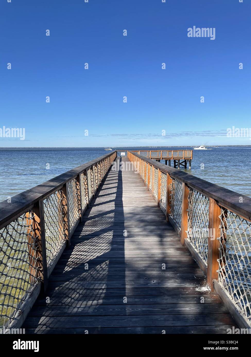 Long wooden pier over the Choctawhatchee Bay Florida with boats on the water - Smartphone Captured Stock Image