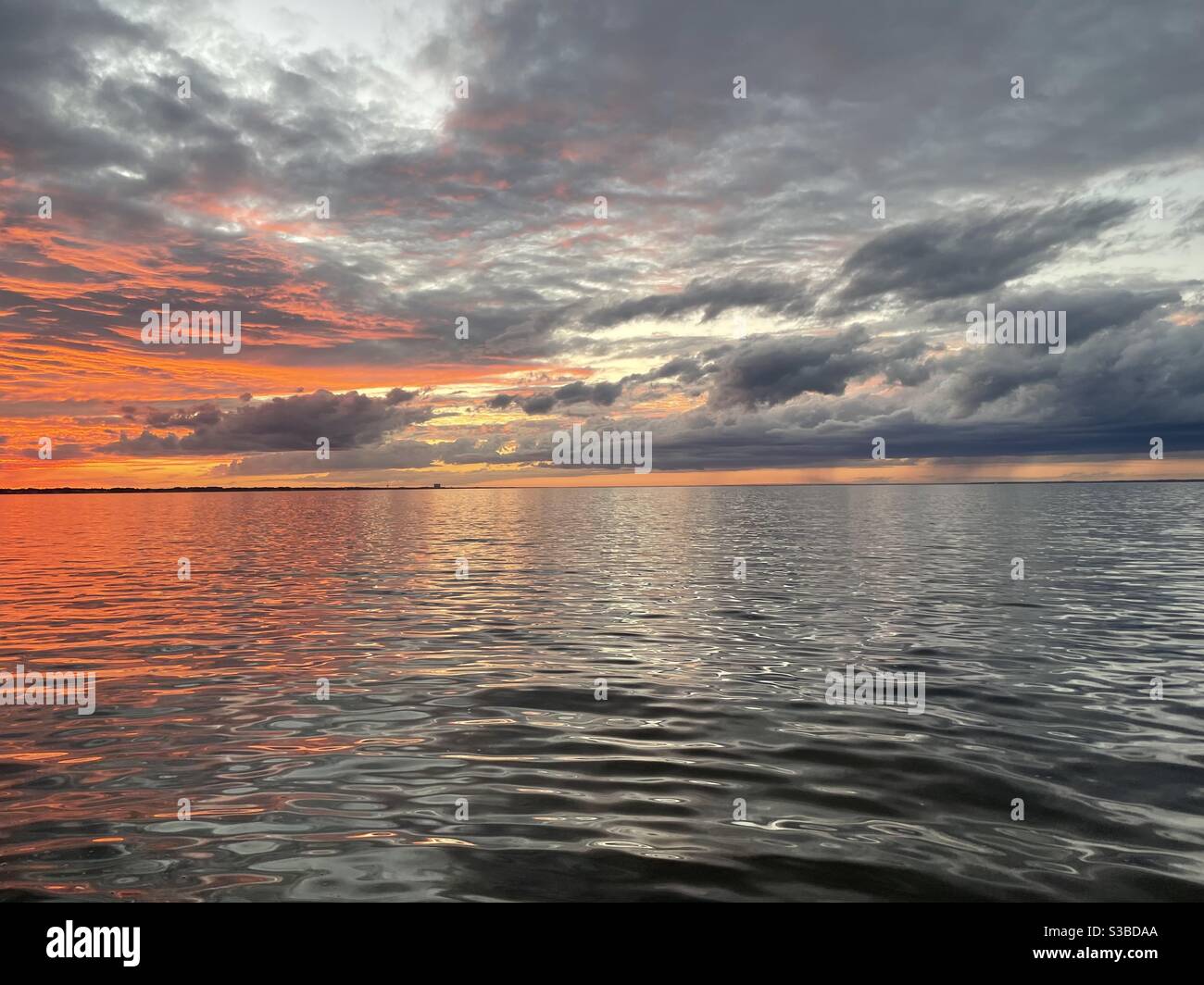 Late colorful sunset skies with clouds and reflections onto bay water ...