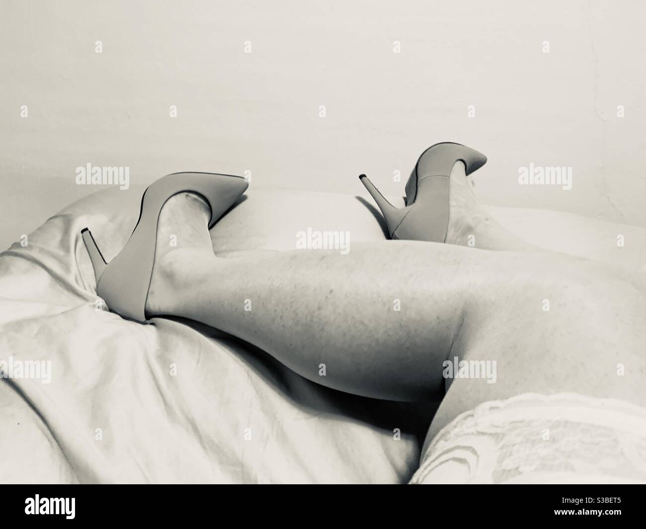 Black and white image of a woman’s legs in thigh-high stockings and high heels as she lies on a bed - Smartphone Captured Stock Image