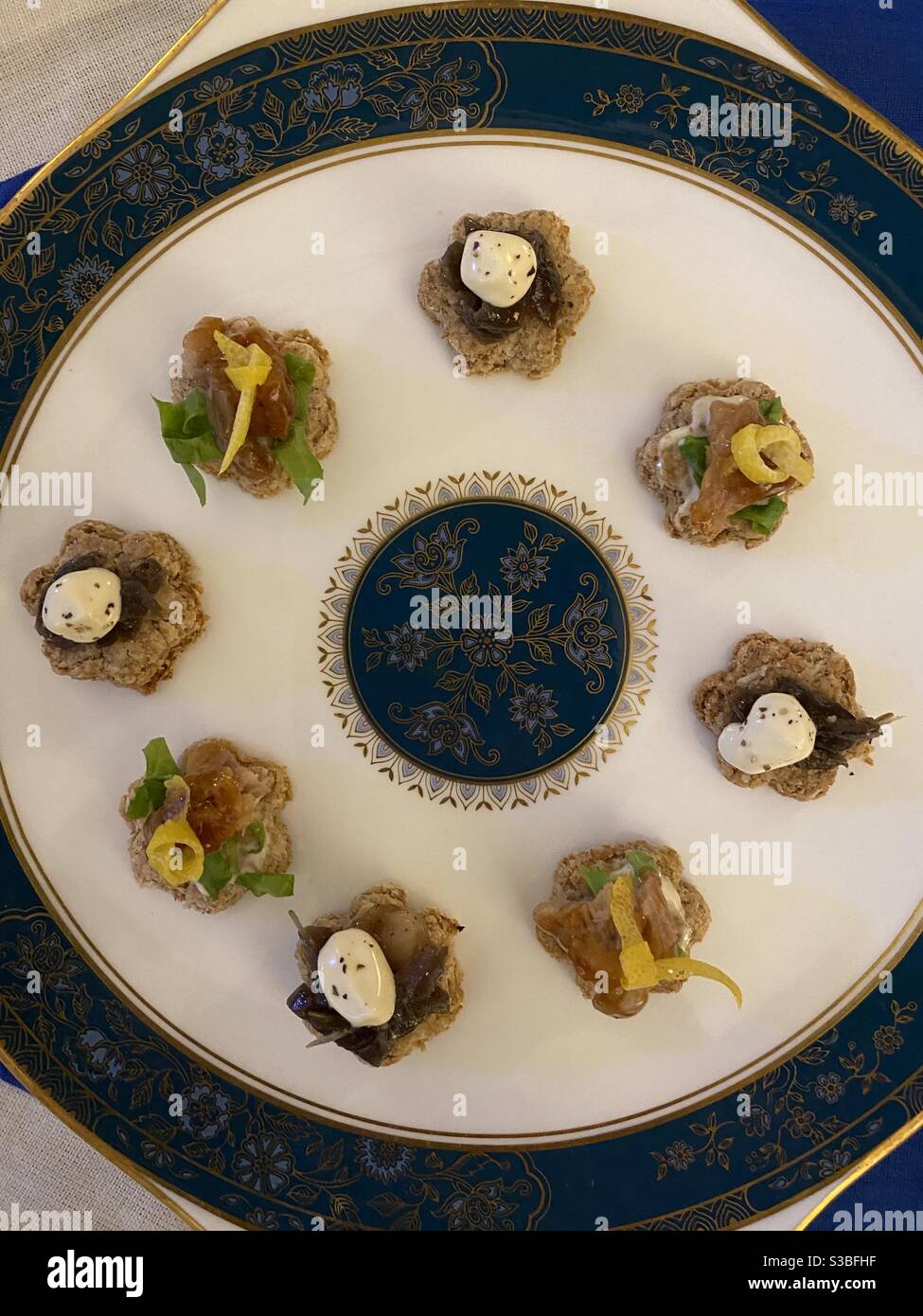 Two varieties of canapés presented on a Royal Doulton plate. Caramelised onion topped with sour cream and black pepper;smoked eel with lettuce shreds and lemon zest knot, both in homemade oatcakes. Stock Photo