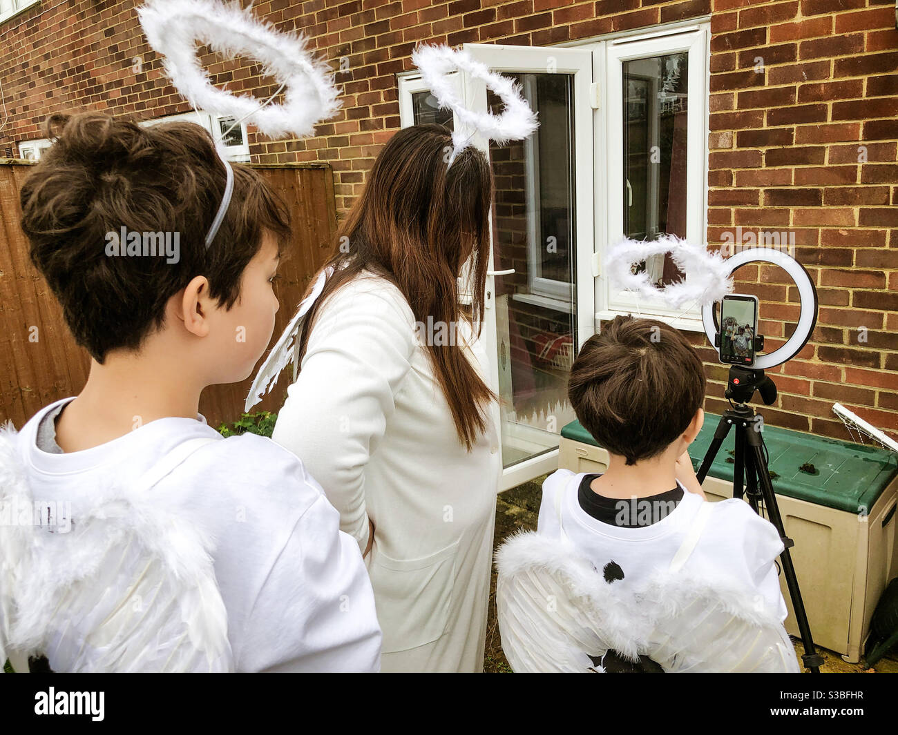 A family dressed up as angels record a scene on a mobile phone as part of a nativity play during Covid-19 lockdown. - Smartphone Captured Stock Image