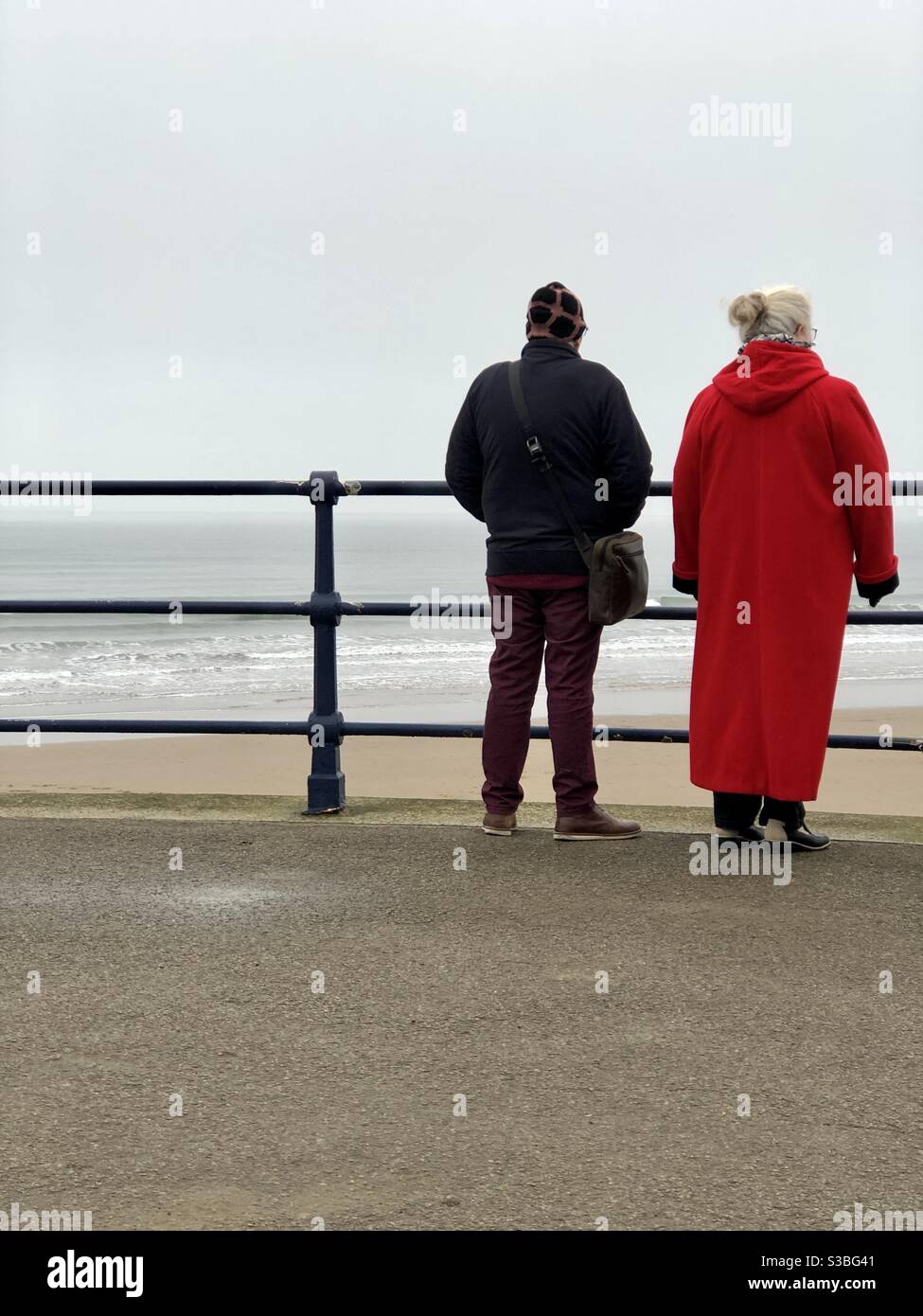 Couple watching waves from the promenade on a winter’s day in the UK - Smartphone Captured Stock Image