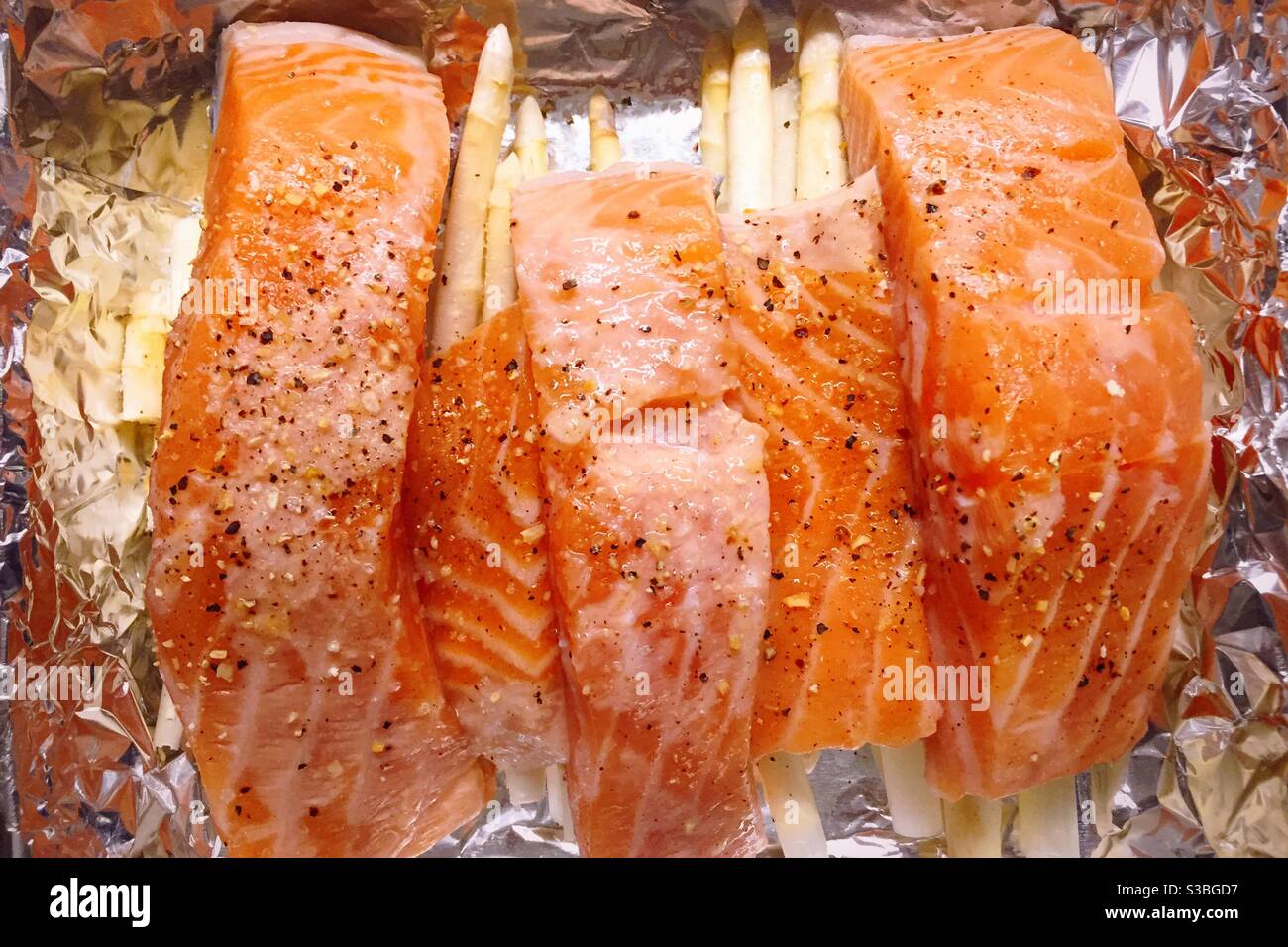 Fillets of salmon on a bed on white asparagus in an aluminum foil covered pan ready to go in the oven - Smartphone Captured Stock Image