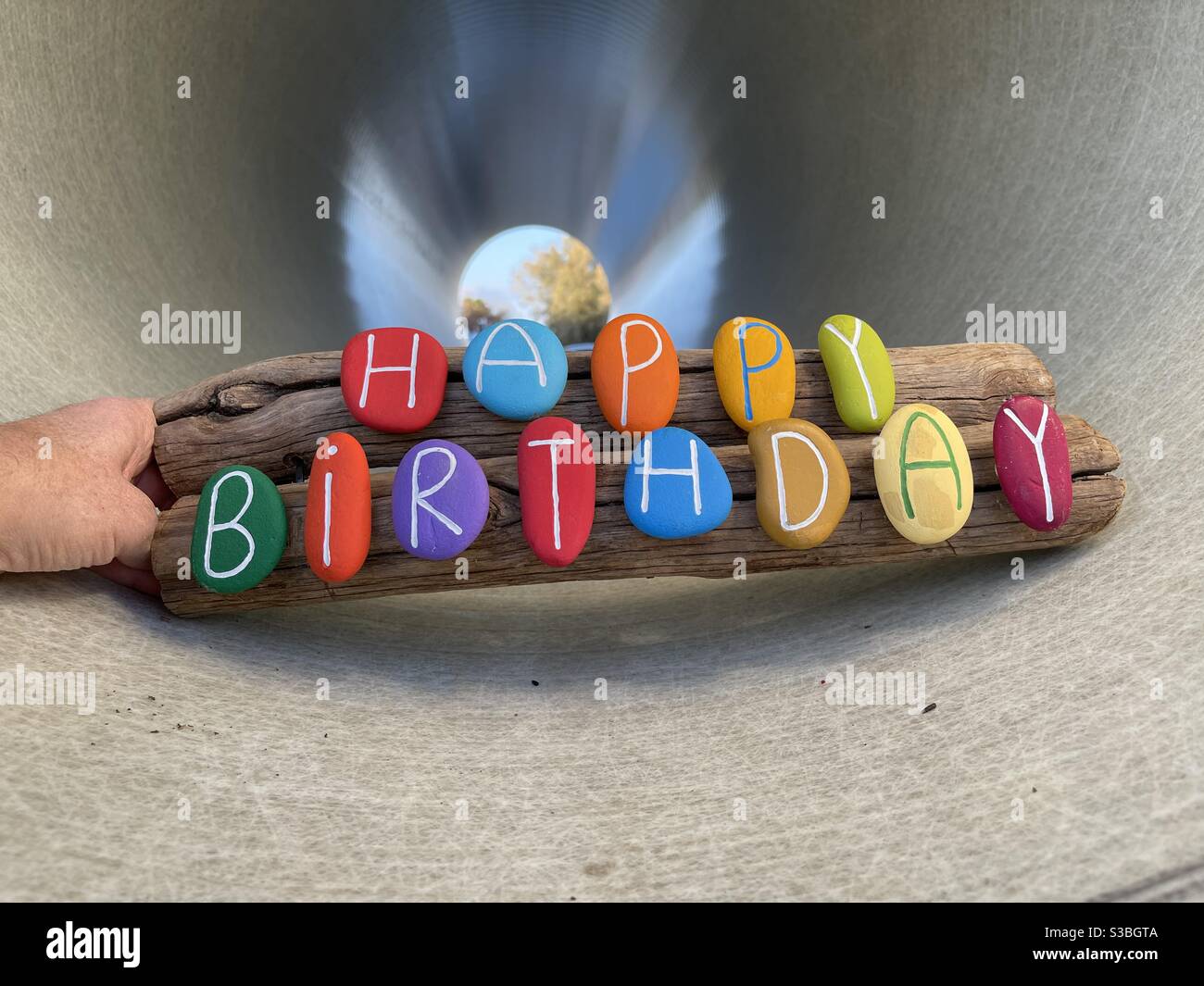 Happy birthday text composed with multi colored stone letters on two wooden pieces in a tunnel - Smartphone Captured Stock Image