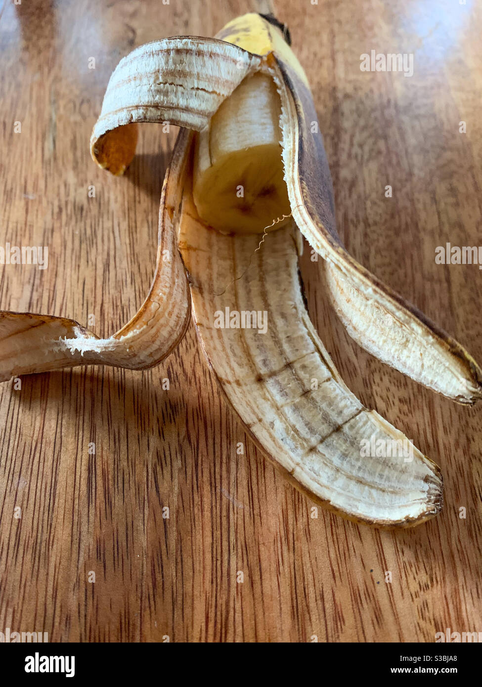 Half a banana in its peel on a wooden table - Smartphone Captured Stock Image