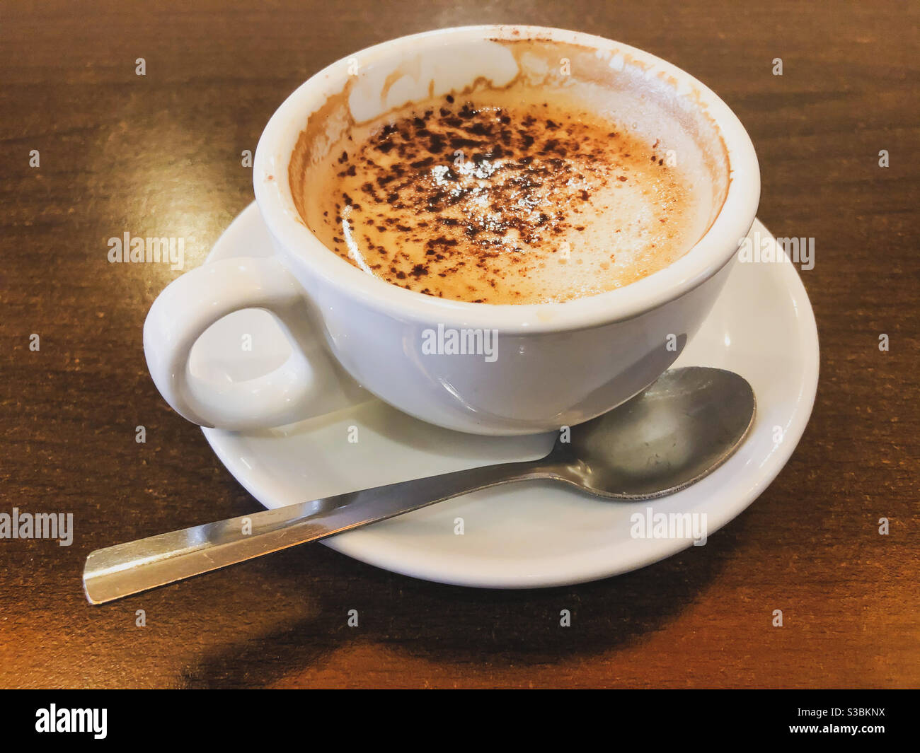 A half drunk cappuccino coffee in a cup on a saucer with a teaspoon. - Smartphone Captured Stock Image