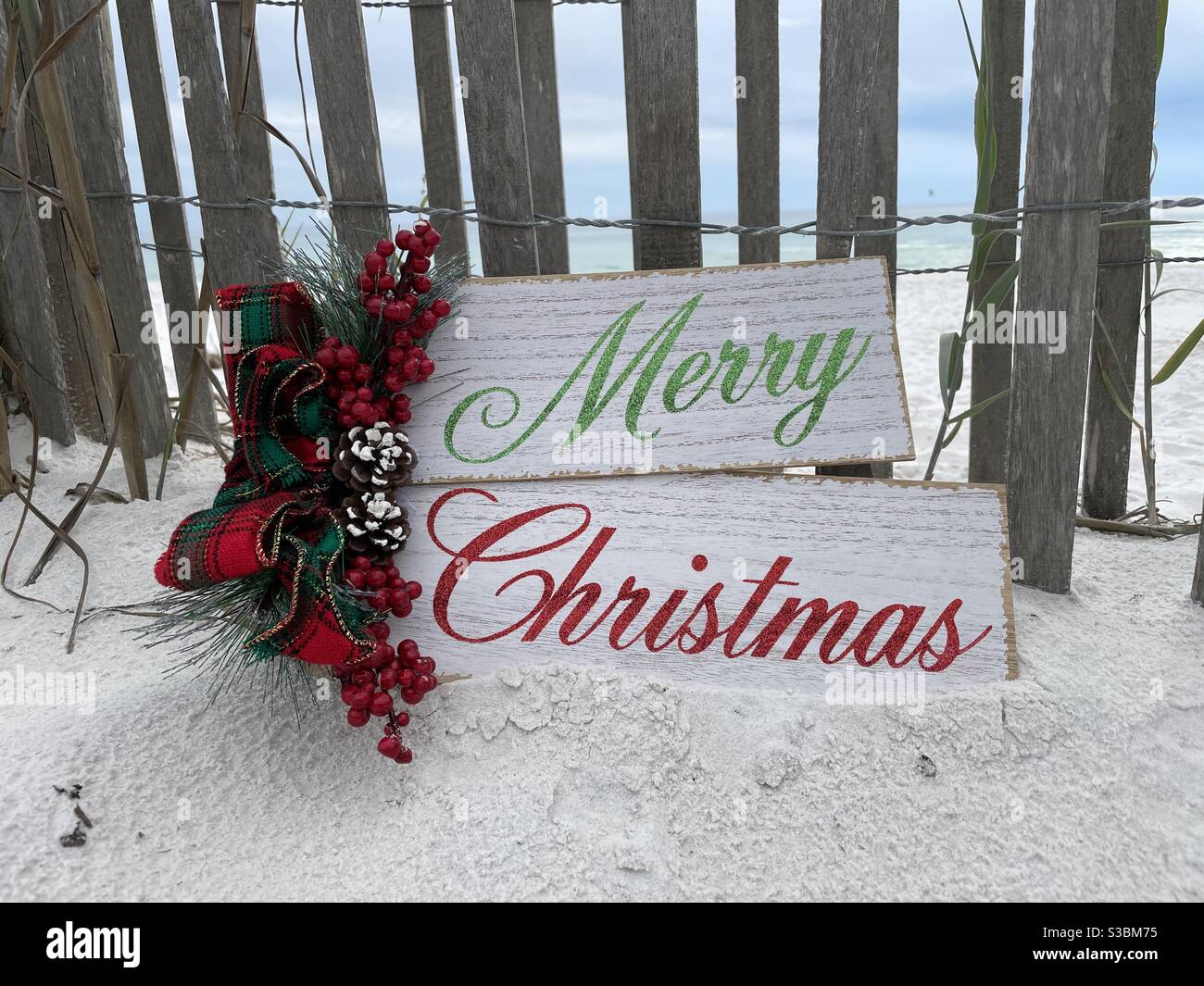 Merry Christmas sign with wooden fence background on white sand Florida beach - Smartphone Captured Stock Image