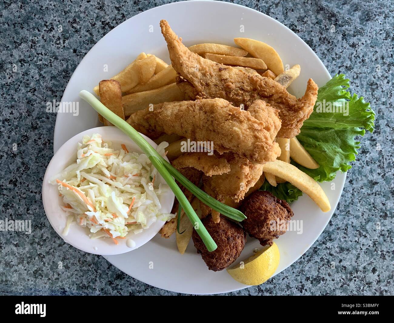 Fried fish, French fried potatoes, corn fritters and Cole slaw on a plate. - Smartphone Captured Stock Image
