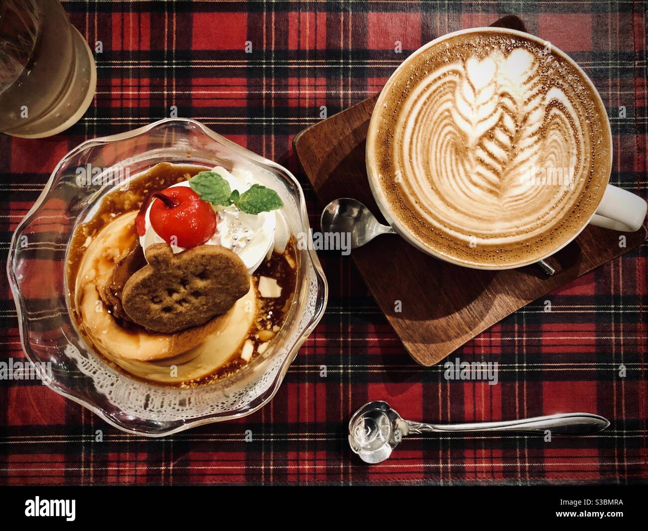 Pudding with whipped cream and a cherry, latte art coffee on a tartan tablecloth - Smartphone Captured Stock Image