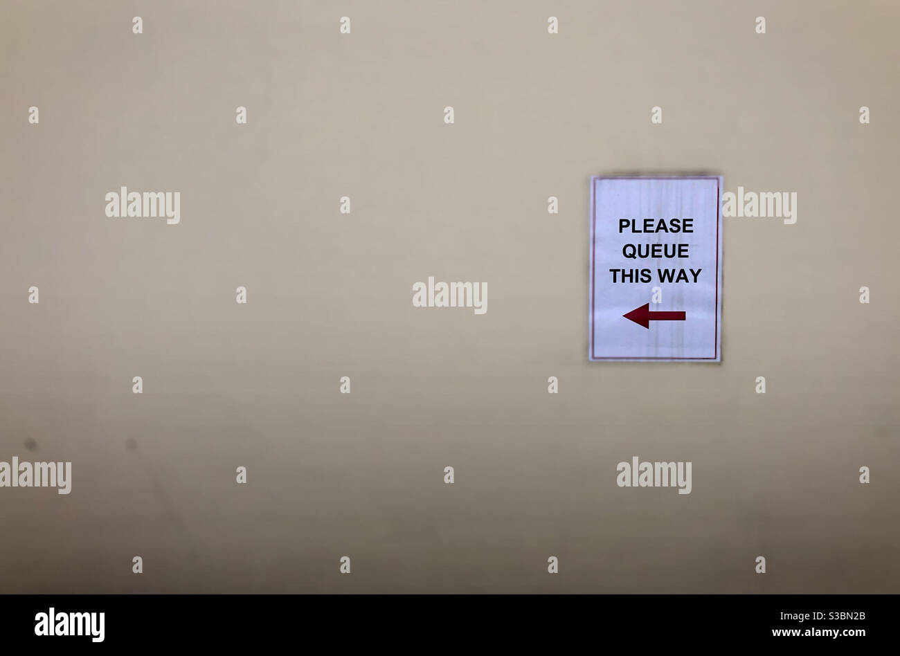 Please Queue This Way sign on a wall Stock Photo Alamy
