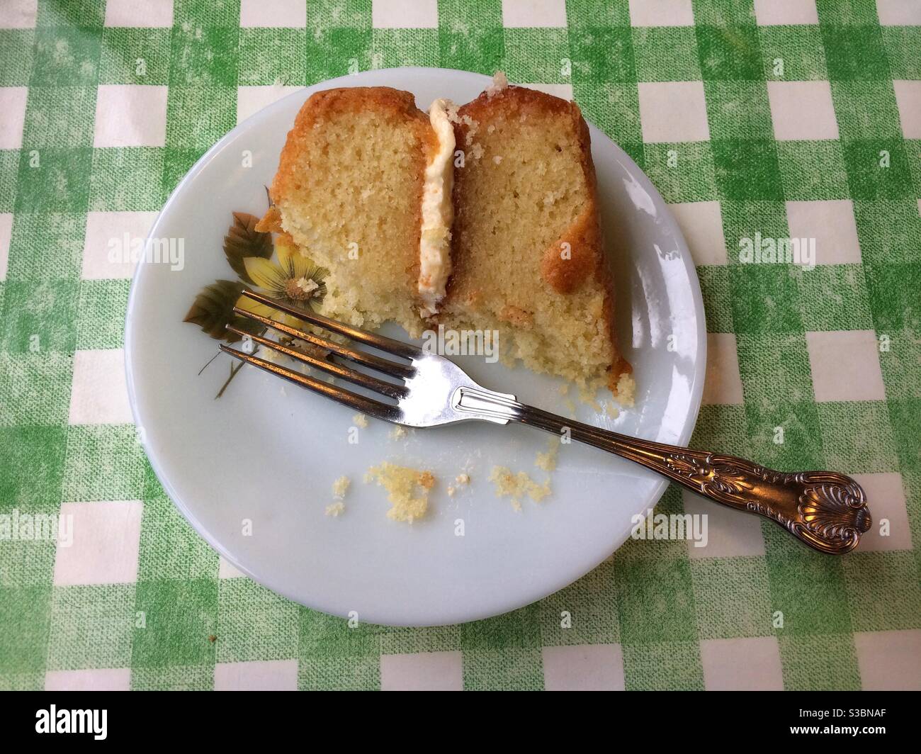 Half eaten Victoria sponge cake on a pretty plate with a green gingham tablecloth, flat lay Stock Photo