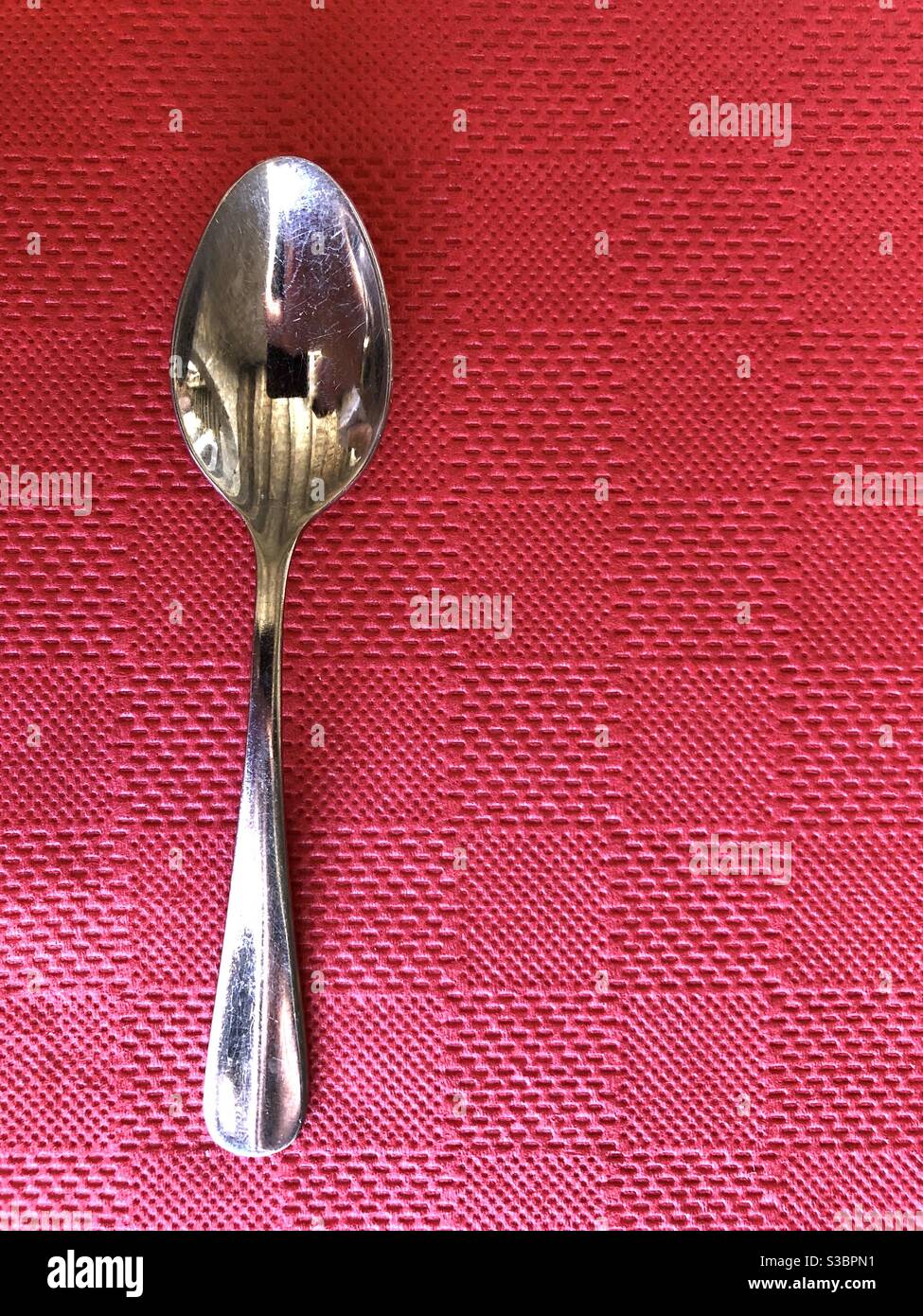 Spoon on a red paper tablecloth background - Smartphone Captured Stock Image