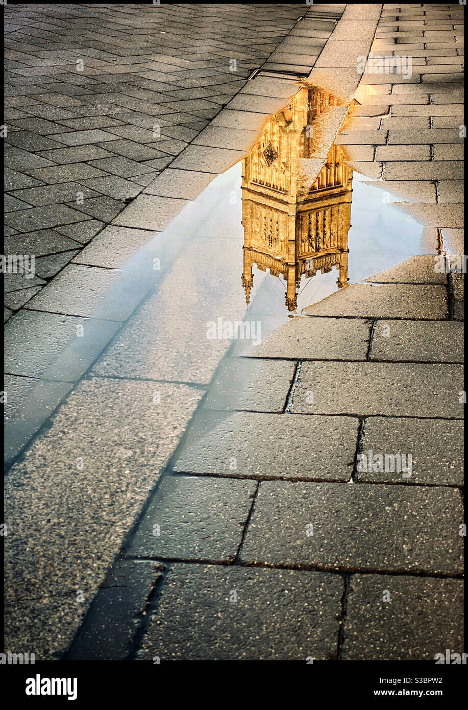 An English church bell tower is reflected in a puddle, somewhere in the Cotswolds region. Photo Credit - ©️ COLIN HOSKINS. Stock Photo