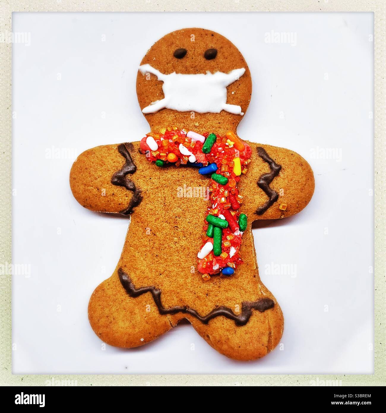 A homemade gingerbread man cookie is decorated with a colorful candy scarf and a face mask. Stock Photo