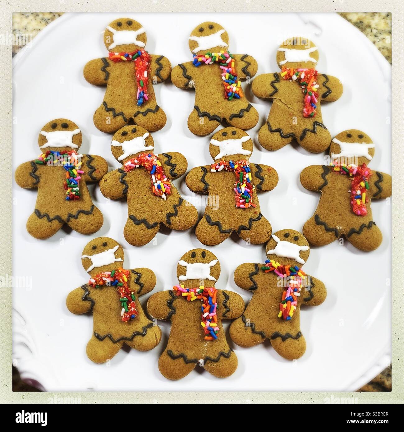 A plate of homemade gingerbread cookies is decorated with colorful candy scarves and face masks. Stock Photo