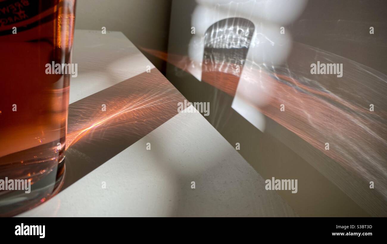 Patterns of light created by sunlight coming through a window blinds and through a glass of red liquid, refracting across white table and wall to create abstract background - Smartphone Captured Stock Image Patterns of light created by sunlight coming through a window blinds and through a glass of red liquid, refracting across white table and wall to create abstract background - Smartphone Captured Stock Image