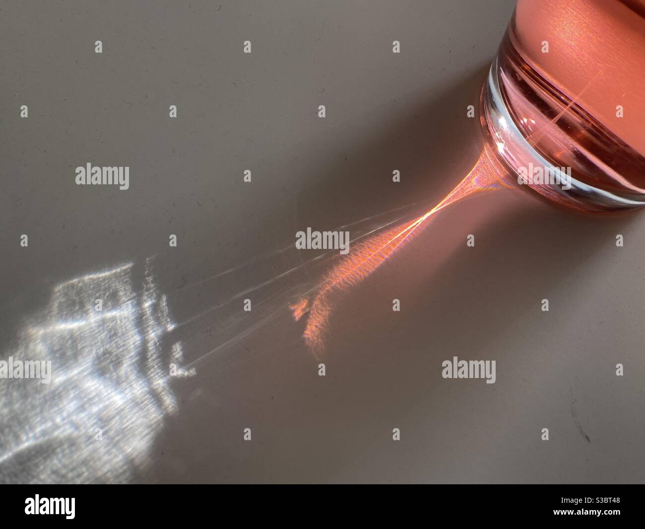 Pattern of light and shadow as sunlight passing through glass of red liquid, refracting across white table and wall, creating abstract background - Smartphone Captured Stock Image Pattern of light and shadow as sunlight passing through glass of red liquid, refracting across white table and wall, creating abstract background - Smartphone Captured Stock Image