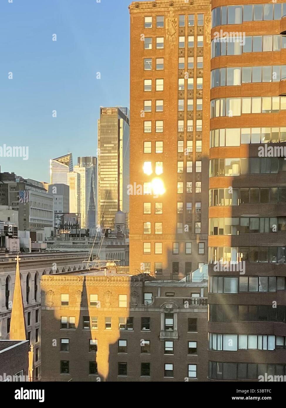 The reflection of the morning sun on the window of a Manhattan skyscraper sends a beam of sunlight down into the city. - Smartphone Captured Stock Image