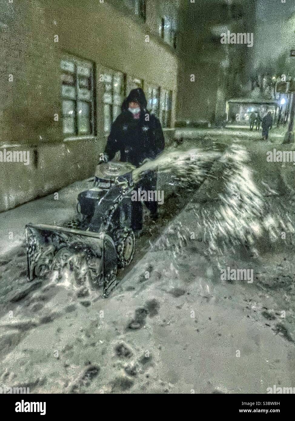 Keeping sidewalks safe. Worker blowing snow off Park Avenue sidewalk near 36th St facing north toward Grand Central Station as a snowstorm builds in Manhattan, Wrapping up 2020 with a White Christma! Stock Photo