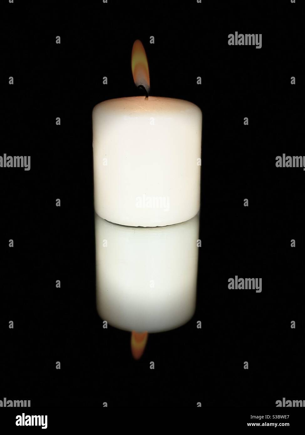 Candle burning with black background on a mirrored surface - Smartphone Captured Stock Image