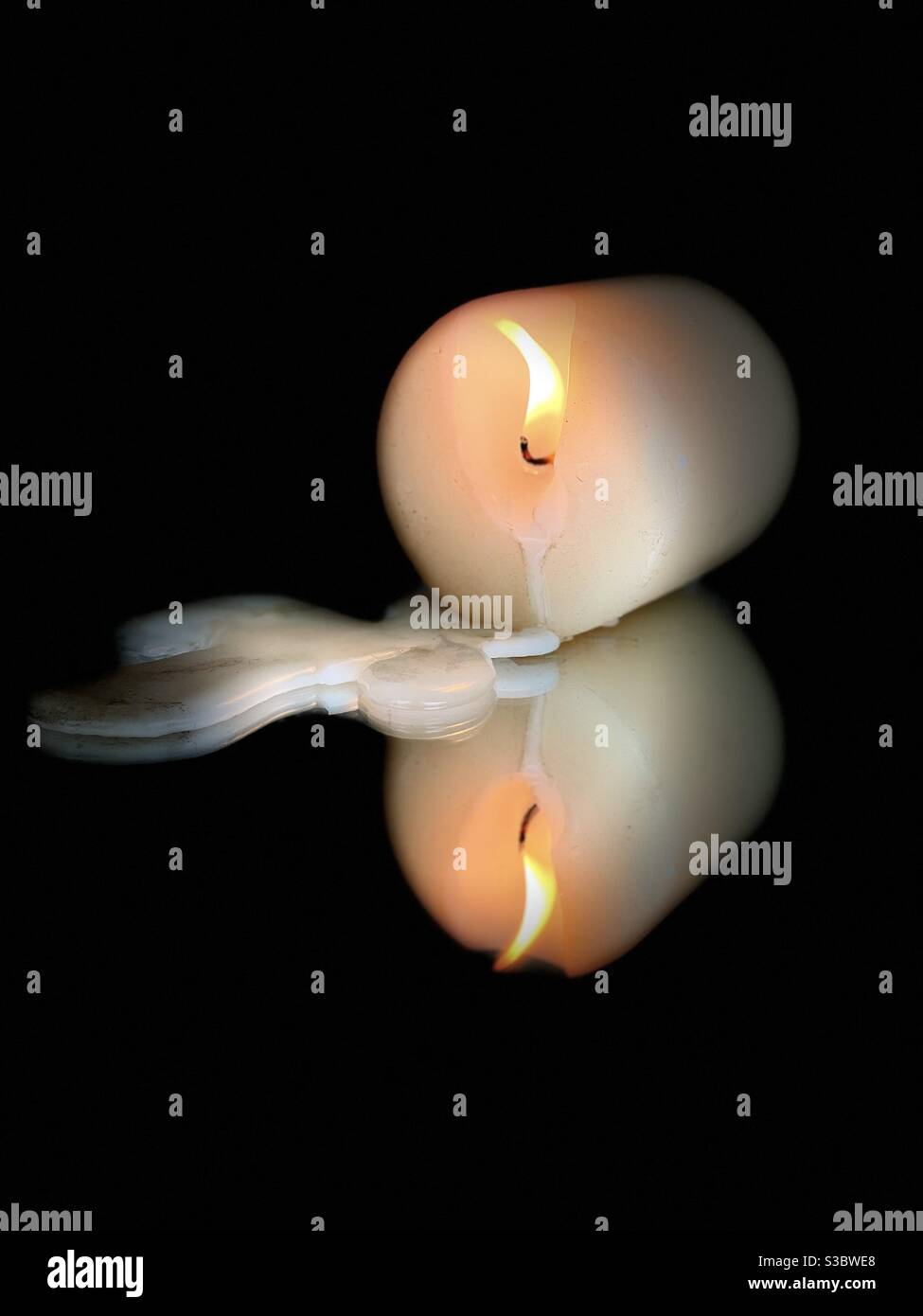 Candle burning with dripping wax on a black background mirrored surface Stock Photo