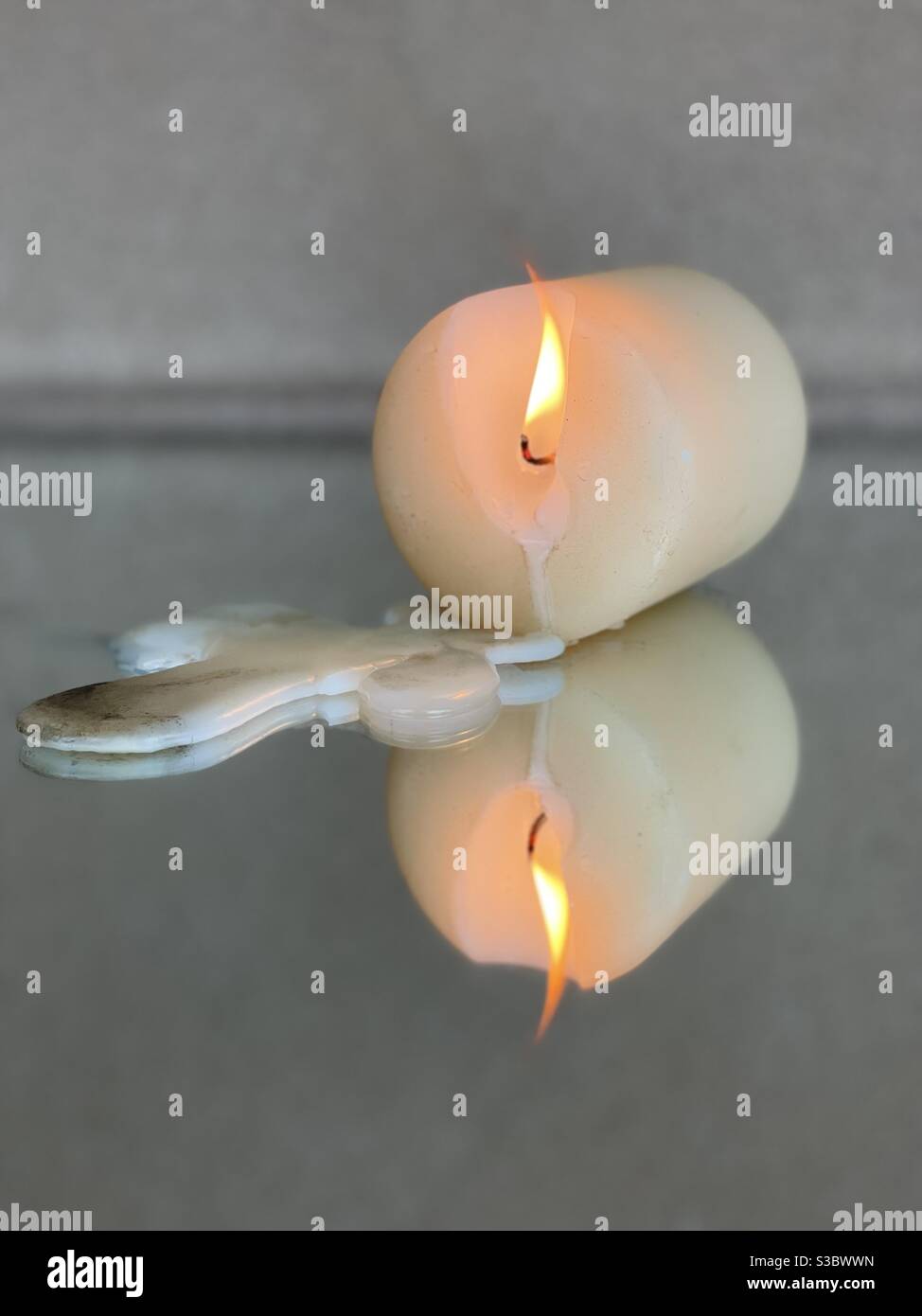 Single candle burning turned sideways with wax drops on mirrored surface Stock Photo