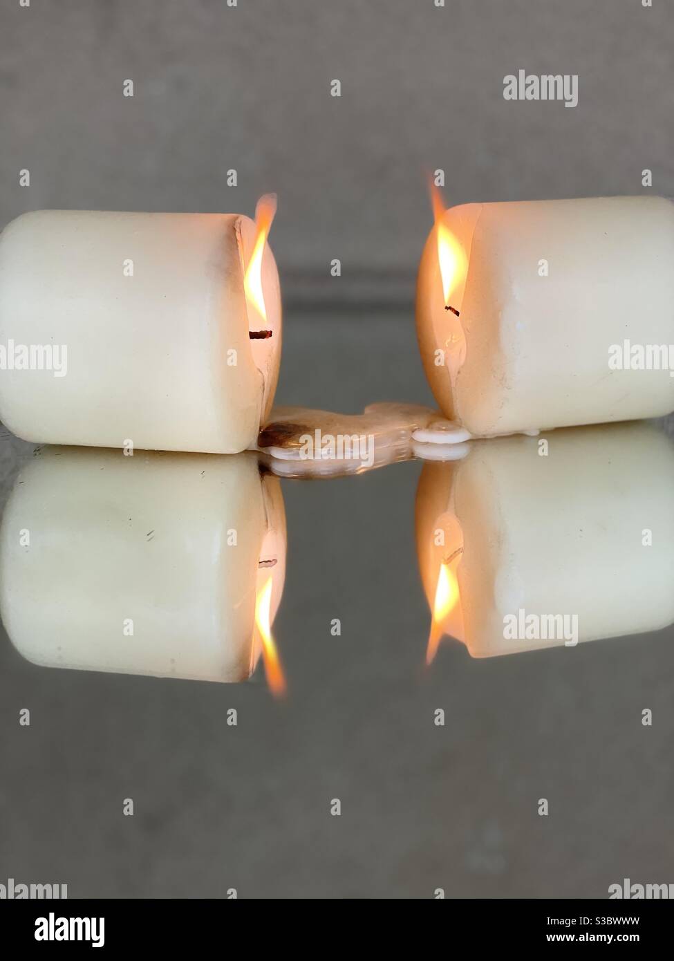 Two burning candles with wax drops on mirrored surface background - Smartphone Captured Stock Image