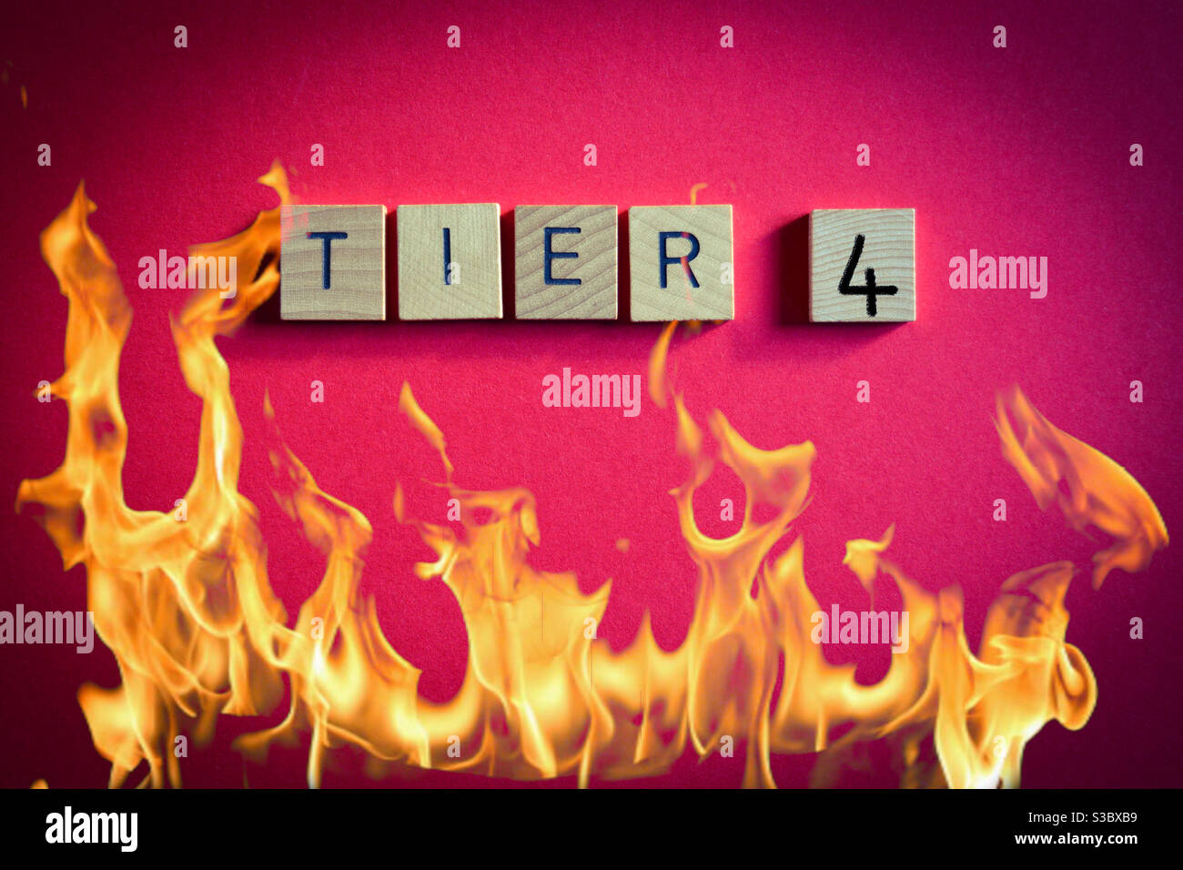 Tier 4, coronavirus alert level, word in wooden alphabet letters isolated on red background with flames - Smartphone Captured Stock Image