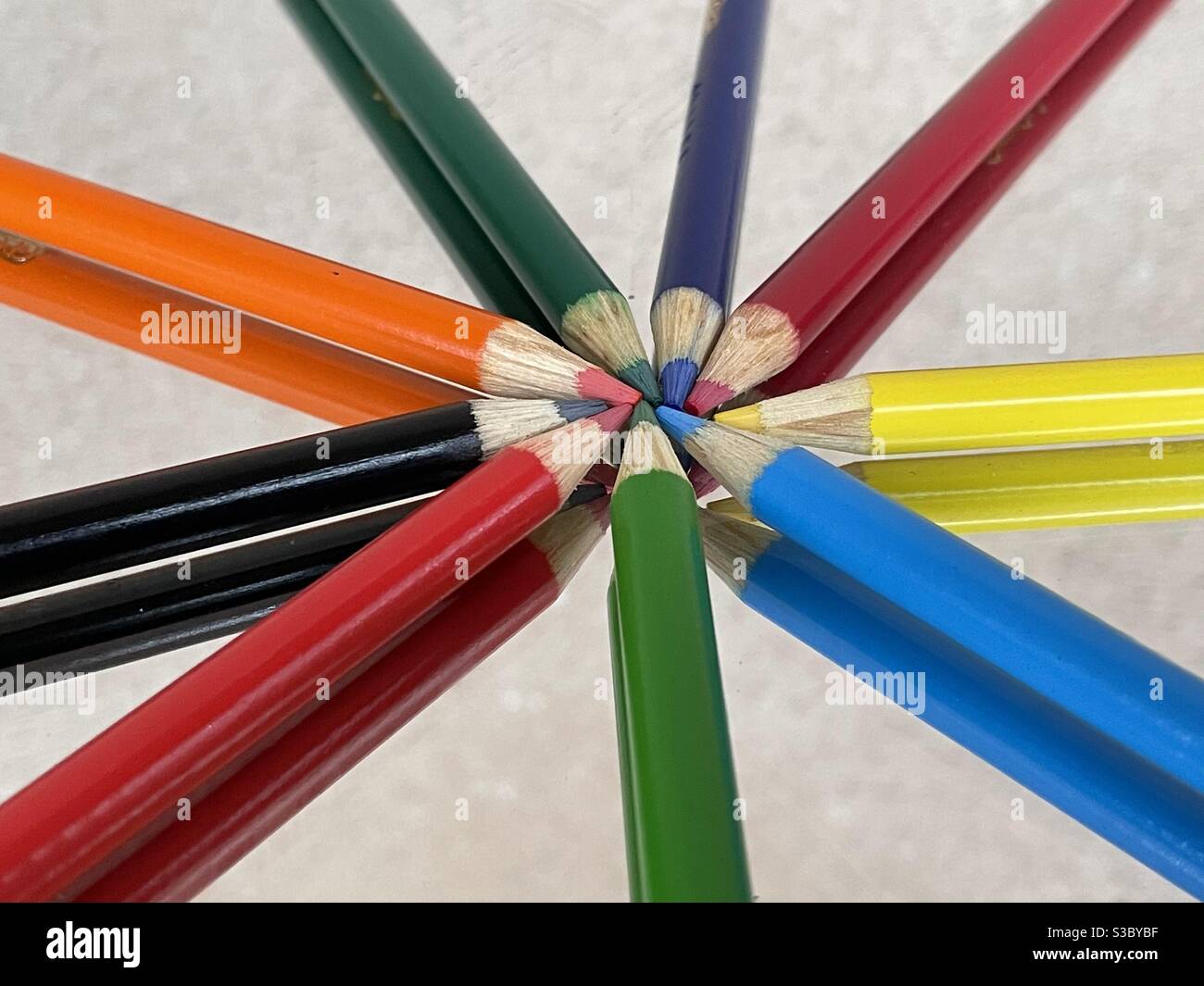 Colorful pencils arranged in a pinwheel on mirrored surface with reflections Stock Photo