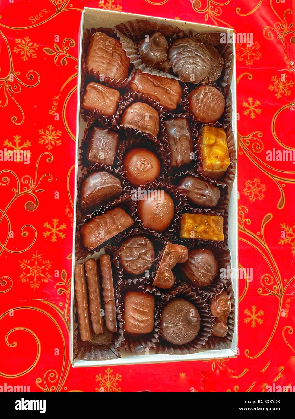 Mouth-watering diet killer assorted chocolate candy against bright red & gold wrapping paper for a holiday treat sugar lovers crave. - Smartphone Captured Stock Image
