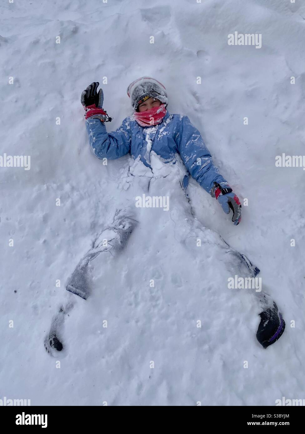 An eight year old girl covered in snow playing outside in winter time fun Stock Photo