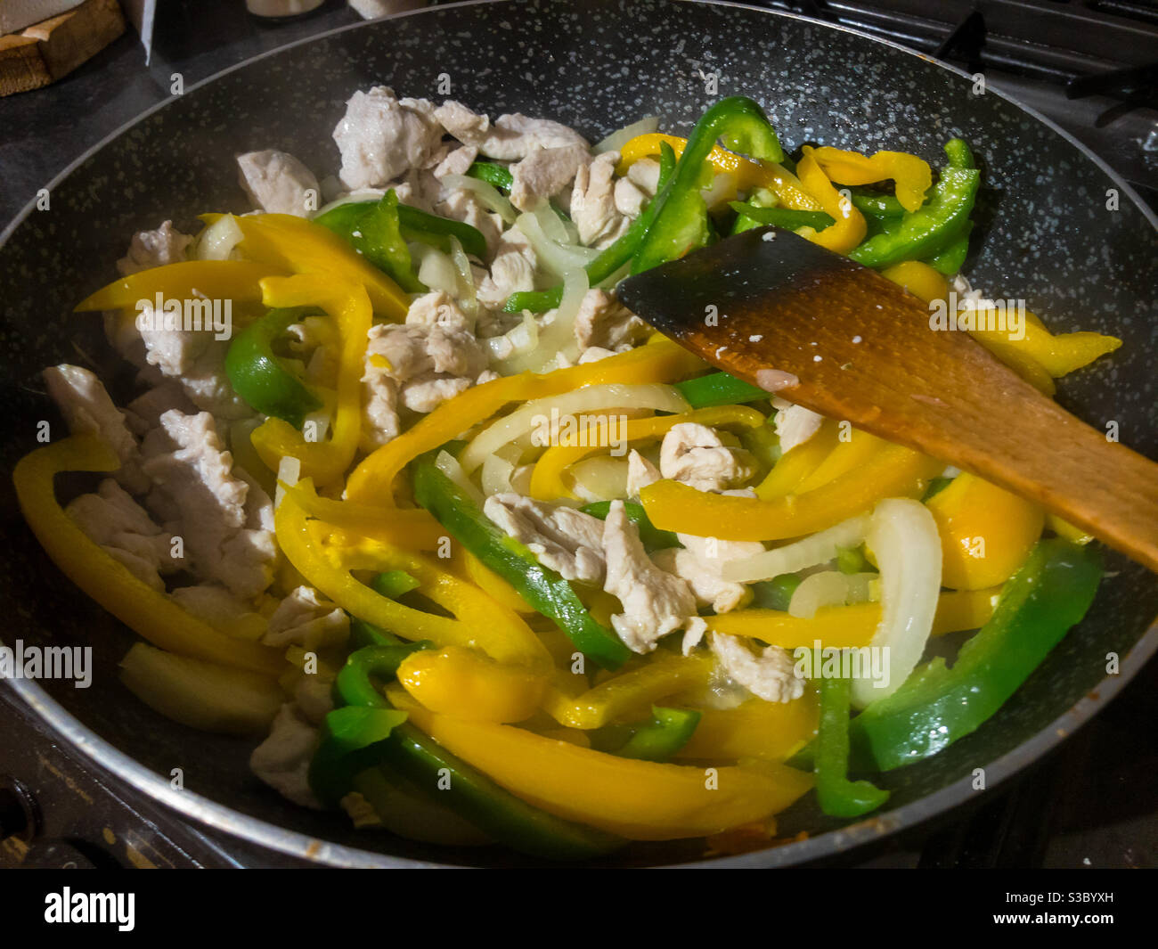 Stir frying sliced chicken, yellow and green peppers, and onions in a wok. Stirring with a wooden spatula. - Smartphone Captured Stock Image Stir frying sliced chicken, yellow and green peppers, and onions in a wok. Stirring with a wooden spatula. - Smartphone Captured Stock Image