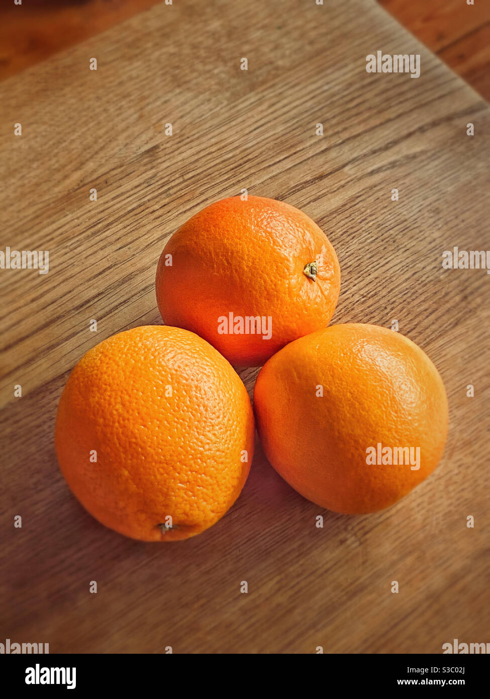 A group of three enticing oranges lye on a wooden table top. A simple but graphic image. Room for copy. Photo Credit - ©️ COLIN HOSKINS. - Smartphone Captured Stock Image