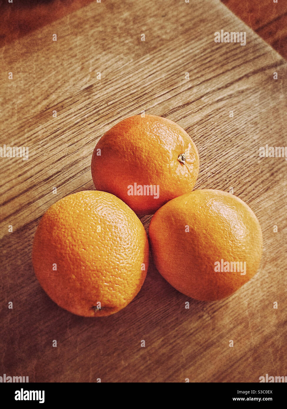An atmospheric image of three oranges clumped together on a wooden table top. Space for copy. Graphic shapes. Photo Credit - ©️ COLIN HOSKINS. - Smartphone Captured Stock Image