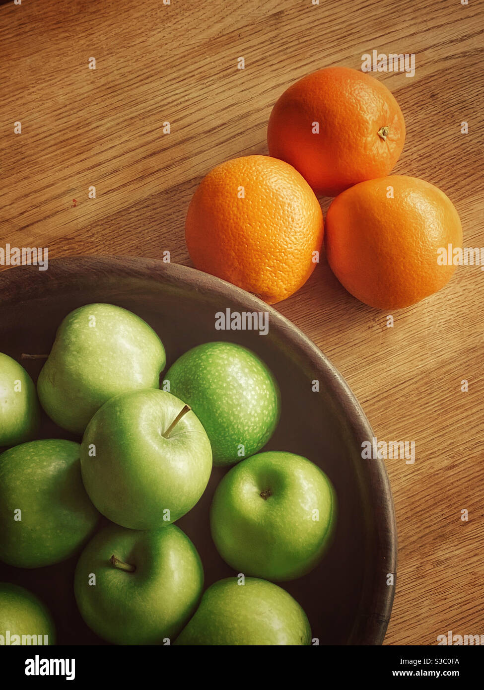 A wooden fruit bowl filled with Green Granny Smith Apples & next to a group of 3 oranges. Fruit means healthy eating & a balanced diet. Photo Credit - ©️ COLIN HOSKINS. - Smartphone Captured Stock Image